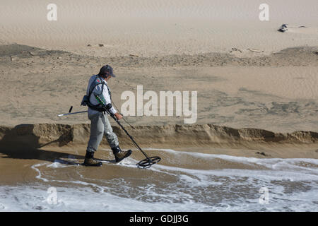 Un maschio solitario utilizzando un rivelatore di metallo lungo la linea di galleggiamento a Huntington Beach in California Foto Stock