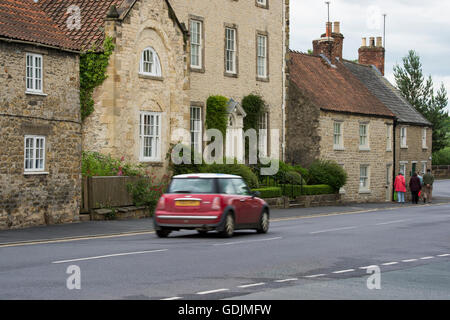 Helmsley, North Yorkshire - Mini Cooper guidando lungo Bridge Street (A170) passando suggestive e storiche case e case. Foto Stock