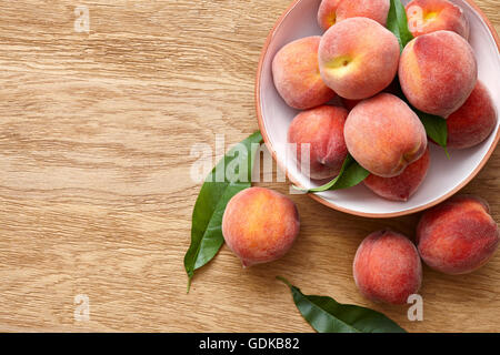 Mature le pesche in una ciotola su sfondo di legno Foto Stock
