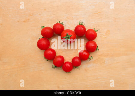 Pomodoro ciliegino fresco nella forma di cuore sul tagliere di legno, laici piatta Foto Stock