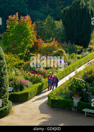 Vista guardando verso il basso sul percorso attraverso giardini formali con estate frontiere e basse siepi con coppia camminando sulla ghiaia Foto Stock