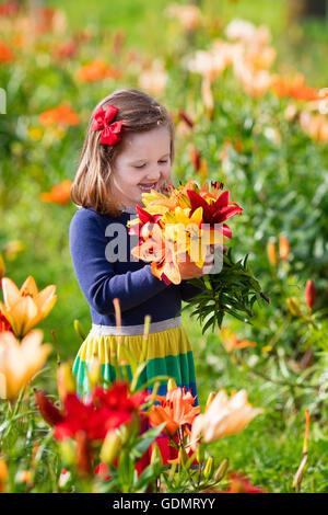 Carino bambina picking lily fiori in fiore giardino d'estate. Bambino azienda bouquet di gigli in fiore bellissimo campo. Foto Stock