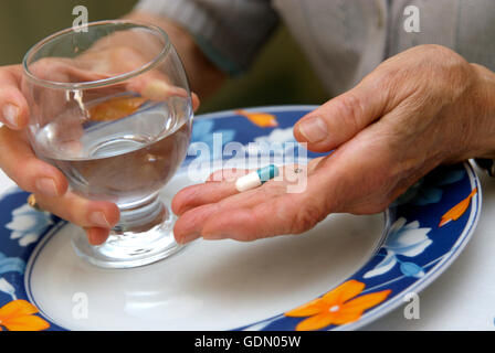 Le mani di una donna anziana tenendo una pillola e un bicchiere di acqua Foto Stock