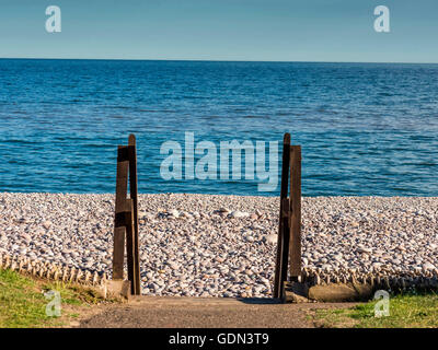 Estate Mare Scena raffigurante spiaggia ghiaiosa con legno gateway di accesso con il blu del mare e del cielo sullo sfondo. Foto Stock