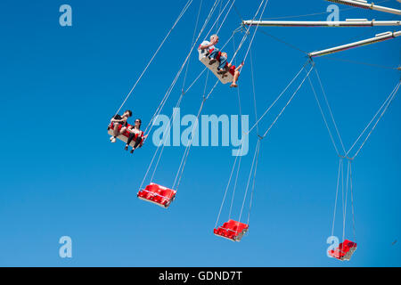 Persone su fairground ride oscilla in alto in aria con un cielo blu sullo sfondo Foto Stock