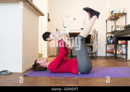 Madre facendo solleva la gamba con il bambino nelle braccia Foto Stock