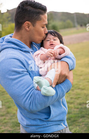 Padre cullano e baciare il bambino in posizione di parcheggio Foto Stock