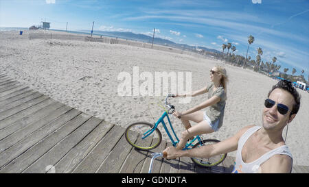 Giovane tenendo selfie escursioni in bicicletta sulla passeggiata a mare di legno della Spiaggia Venice, California, Stati Uniti d'America Foto Stock