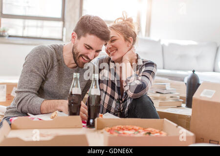 Casa in movimento: Coppia giovane mangiare la pizza nella nuova casa, circondato dalle caselle Foto Stock