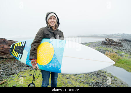 Ritratto di donna surfer che trasportano le tavole da surf a costa, Mare, Oregon, Stati Uniti d'America Foto Stock