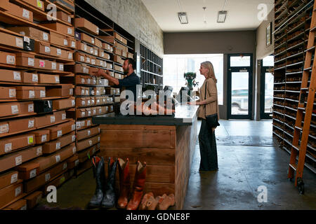 Il comando cobbler selezionando scatola di scarpe per clienti di sesso femminile nel tradizionale negozio di scarpe Foto Stock