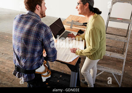 Carpenter e client con blueprint utilizzando laptop Foto Stock