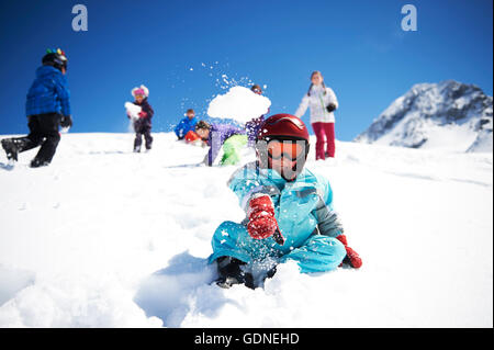 Ragazzo giovane lanciando palle di neve mentre gli amici giocare dietro di lui Foto Stock