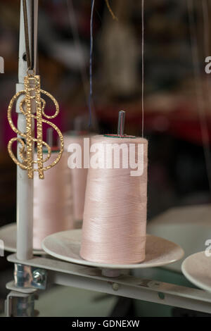 Bobina di filo rosa in una macchina da cucire lo stelo da un golden dollar sign pendente. Foto Stock