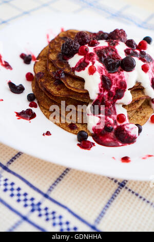 Vista ravvicinata su una pila di frittelle con yogurt e salsa di frutti di bosco, su una piastra bianca Foto Stock