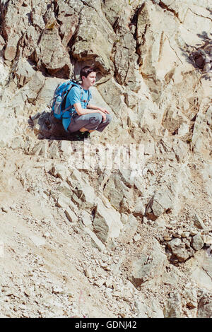 Ragazzo seduto sulla collina rocciosa Foto Stock