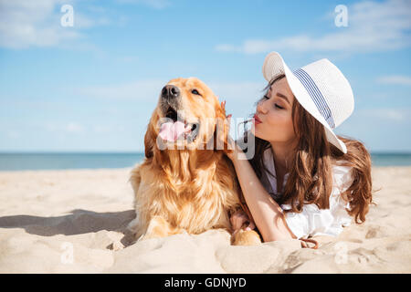 Carino giovane donna divertendosi e provando a baciare il suo cane sulla spiaggia Foto Stock