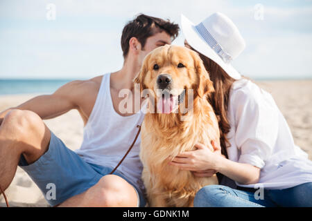Bella coppia Giovane seduto e nascondersi dietro il cane sulla spiaggia Foto Stock