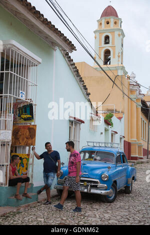 Un auto classica e tre giovani uomini a parlare al di fuori di un negozio in Trinidad, Cuba Foto Stock