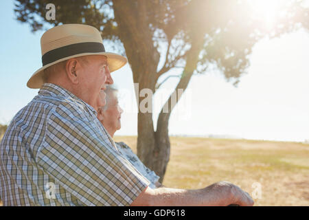 Vista laterale colpo di senior uomo in hat seduti all'aperto con sua moglie e godendo di una vista. Coppia di anziani di relax all'aperto su un su Foto Stock