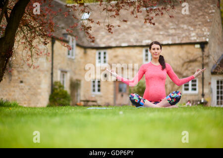 Donna incinta seduti all'aperto in posizione di yoga Foto Stock