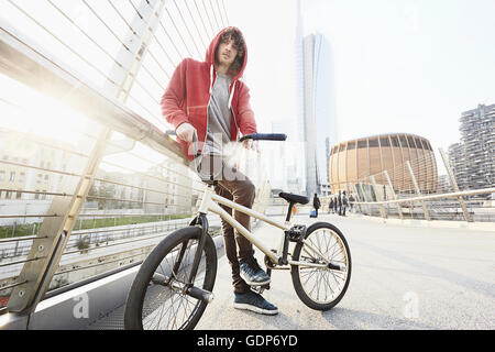 Uomo con la BMX appoggiata contro il corrimano in area urbana Foto Stock