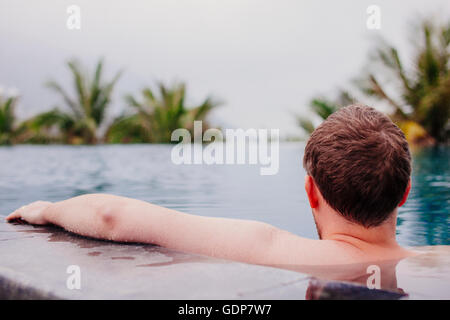 Vista posteriore dell'uomo di balneazione in piscina infinity e guardando fuori di nebbia, Da Nang, Vietnam Foto Stock