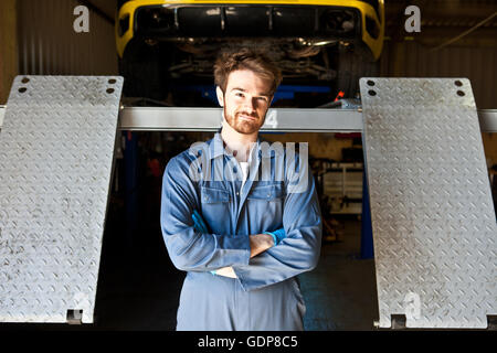 Ritratto di meccanico maschio dietro la macchina di sollevamento in garage Foto Stock