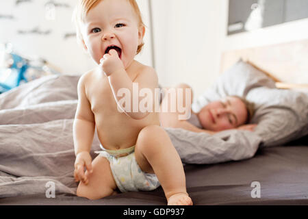 Baby ragazza seduta sul letto con stanco madre Foto Stock