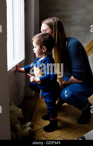 Metà donna adulta e baby figlio guardando attraverso la vita di finestra in camera Foto Stock