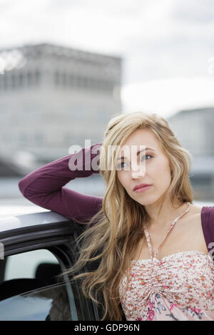 Giovane donna appoggiata contro auto in città Foto Stock