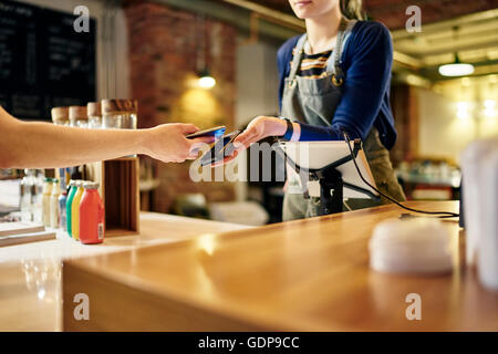 Barista femmina tenendo lo smartphone il pagamento senza contatto da coffee shop il cliente Foto Stock