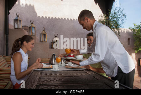 Cameriere che serve coppia giovane prima colazione, Marrakech, Marocco Foto Stock