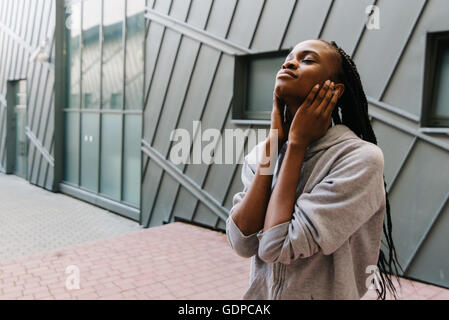 Lo stile di vita e il concetto di persone - sorridente americano africano giovane donna o ragazza adolescente in ascolto in cuffia la musica di chiudere le orecchie con le mani all'aperto Foto Stock