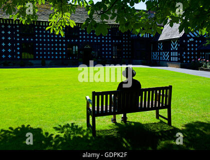 Senior uomo seduto sul banco a Samlesbury Hall, vicino a Preston, Lancashire, Inghilterra, Regno Unito Foto Stock