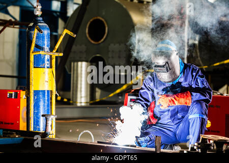 Saldatrice a lavorare in un ambiente industriale di fabbricazione di apparecchiature in acciaio Foto Stock