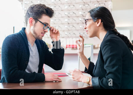 Uomo in ottica di ottenere consigli da commessa l'acquisto di nuovi occhiali Foto Stock