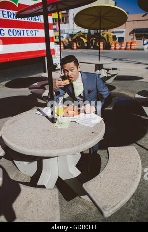 Uomo asiatico che indossa un vestito che mangia un hot dog a New York Foto Stock
