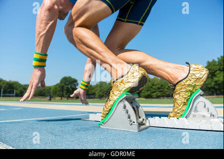 Atleta in oro scarpe a partire una gara in motion blur dai blocchi su un blu acceso via Foto Stock