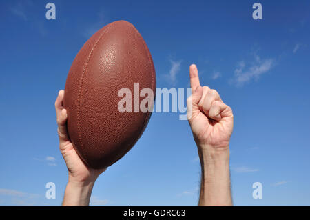 Giocatore di Football Americano celebra un touchdown tenendo un Football Americano e dando un numero unico segno Foto Stock