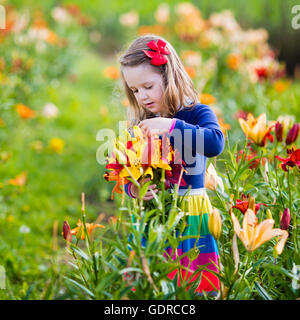 Carino bambina picking lily fiori in fiore giardino d'estate. Bambino azienda bouquet di gigli in fiore bellissimo campo. Foto Stock