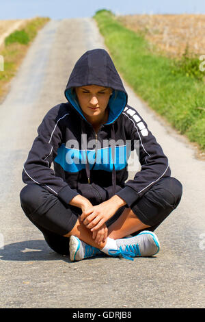 Infelice giovane donna seduta su una strada Foto Stock