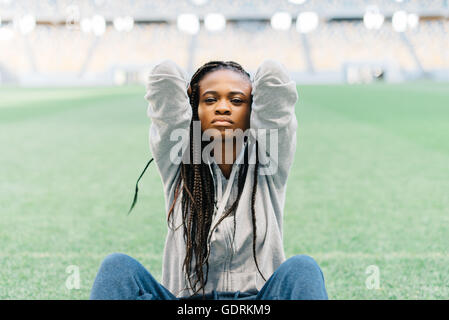 Infelici e frustrati americano africano donna seduta con le mani dietro la testa sull'erba verde Foto Stock