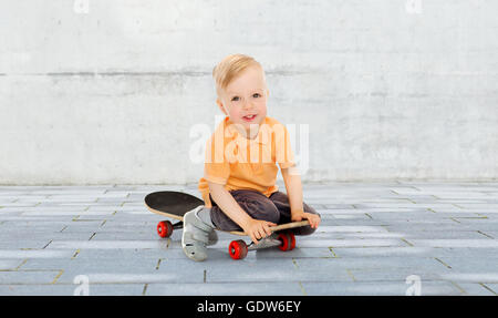 Felice piccolo ragazzo seduto su skateboard Foto Stock