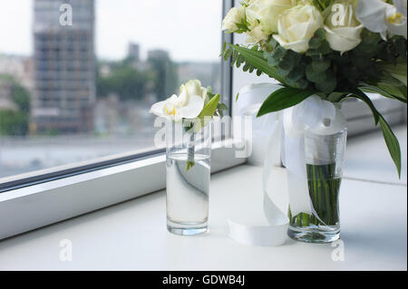 Bellissimo mazzo di nozze in un vaso di vetro. I fiori sul davanzale bianco. Boutonnière in un piccolo vaso. Foto Stock