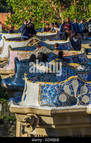 Turisti che si godono la serpentina multicolore banco a Park Guell, Barcellona, in Catalogna, Spagna Foto Stock