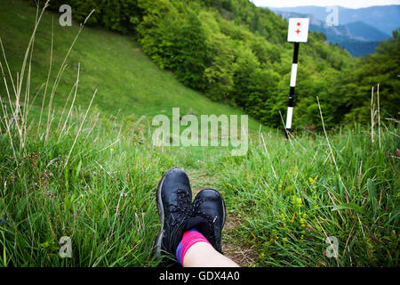 Gambe di donna escursionista seduti sulla cima di una montagna alta al di sopra di una foresta verde. Concetto di libertà Foto Stock