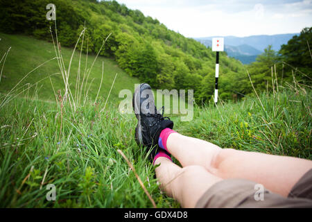 Gambe di donna escursionista seduti sulla cima di una montagna alta al di sopra di una foresta verde. Concetto di libertà Foto Stock