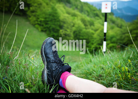 Gambe di donna escursionista seduti sulla cima di una montagna alta al di sopra di una foresta verde. Concetto di libertà Foto Stock