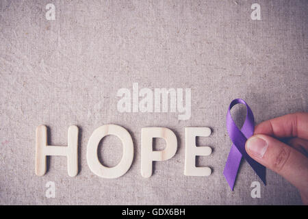 Tenendo le dita viola nastro con speranza la lettera in legno, tonificante, il morbo di Alzheimer, cancro pancreatico, epilessia consapevolezza, Hodgk Foto Stock